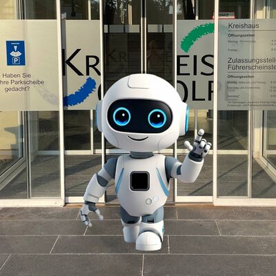 Fotomontage: kleiner wei&szlig;er Roboter schreitet aus der Haupteingangst&uuml;r des Kreishauses, l&auml;chelt und winkt.