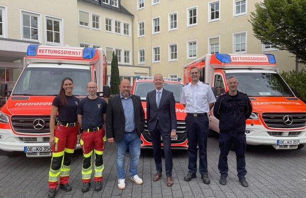 Die Personen stehen vor drei Fahrzeugen: Links und rechts ein RTW, in der Mitte ein NEF.